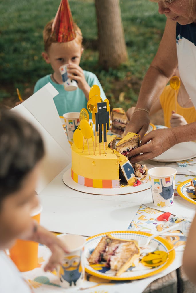 A child is cutting a cake with a yellow hat